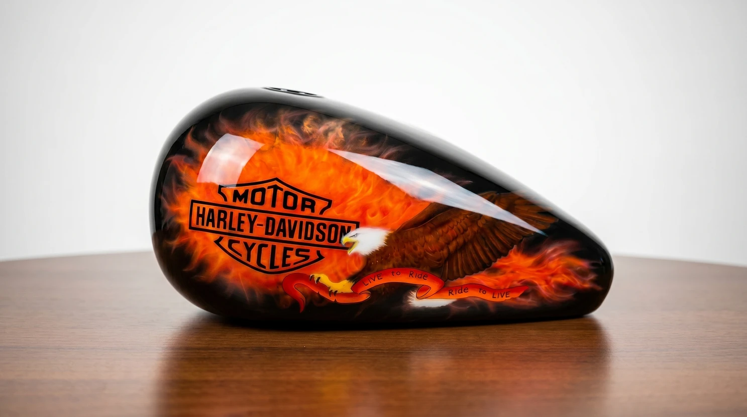 Réservoir de carburant Harley-Davidson posé sur une surface en bois, fond blanc