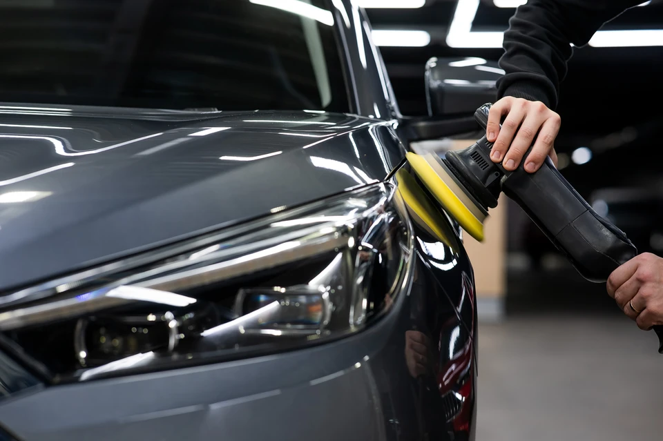 Homme technicien en chemise bleue appliquant un produit d'étanchéité ou mastic sur la carrosserie d'un véhicule beige dans un atelier automobile