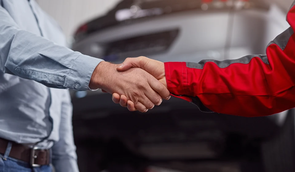 Scène en intérieur d'atelier automobile avec technicien effectuant nettoyage détaillé de carrosserie