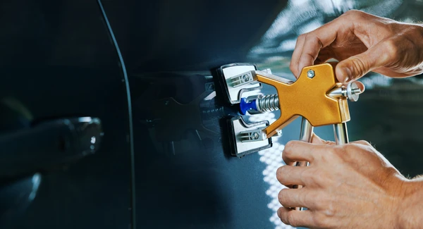 Intérieur d'atelier automobile, technicien en gants noirs utilisant une polisseuse orbitale électrique sur carrosserie blanche de véhicule