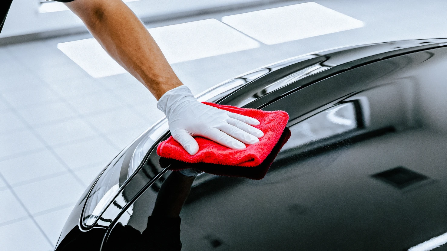 Cabine de peinture automobile professionnelle avec ouvrier en combinaison de protection intégrale appliquant de la peinture rouge au pistolet sur véhicule
