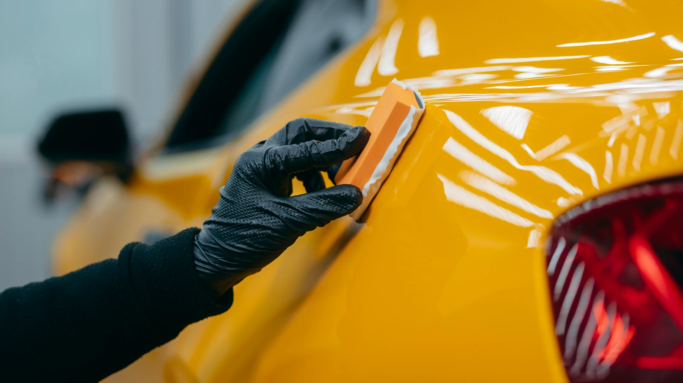 Atelier de carrosserie automobile avec technicien en combinaison de protection intégrale appliquant de la peinture au pistolet sur véhicule