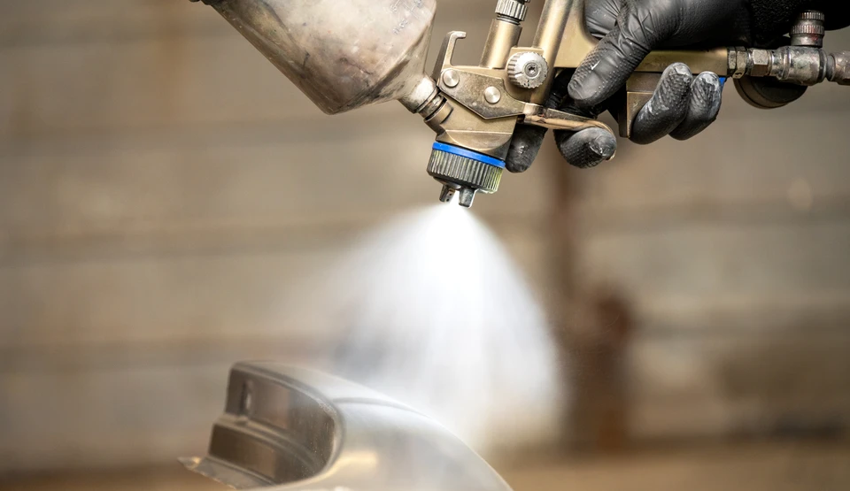 Atelier de carrosserie automobile avec technicien en combinaison de protection appliquant de la peinture blanche sur véhicule