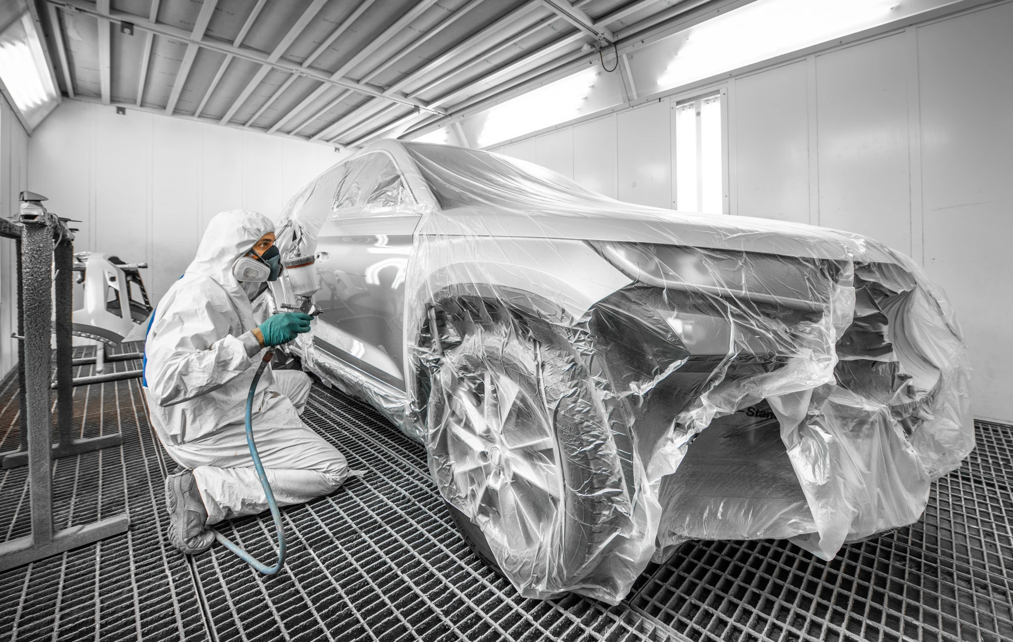 Cabine de peinture automobile professionnelle avec ouvrier en combinaison de protection intégrale appliquant de la peinture rouge au pistolet sur véhicule