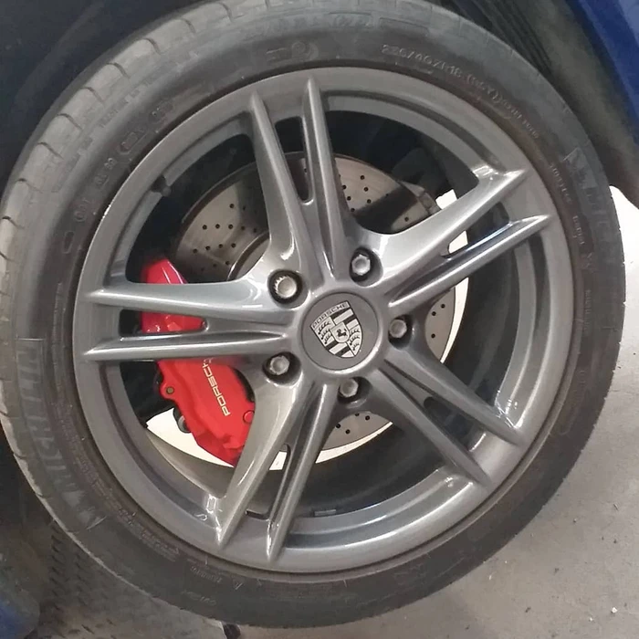 Atelier de peinture industrielle avec ouvrier appliquant une finition au pistolet à peinture sur une pièce automobile grise montée sur support de rotation