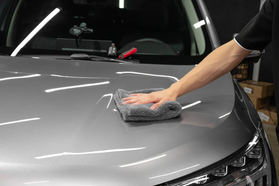 Carrossier expérimenté en salopette professionnelle dans son atelier, inspectant minutieusement la carrosserie repeinte d'une voiture à l'aide d'une lampe de diagnostic, démontrant la maîtrise technique et l'attention au détail de la finition. L'atelier moderne doit être visible en arrière-plan avec équipements de peinture et de débosselage professionnels. La scène doit transmettre la rigueur, la spécialisation et l'expertise en carrosserie-peinture.